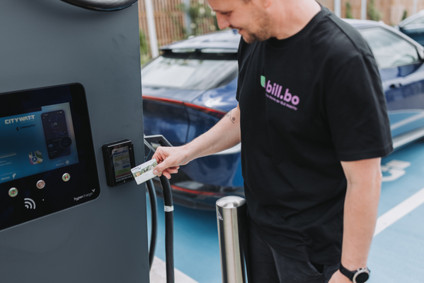 Eine Person bezahlt an einer Ladestation für Elektrofahrzeuge mit einer Karte.