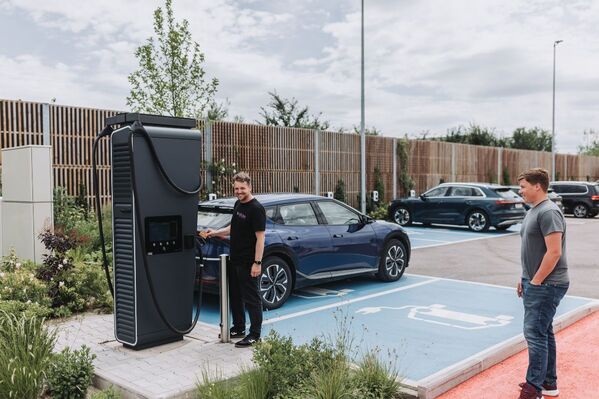 Zwei Personen stehen in der Nähe einer Ladestation für Elektroautos auf einem Parkplatz.