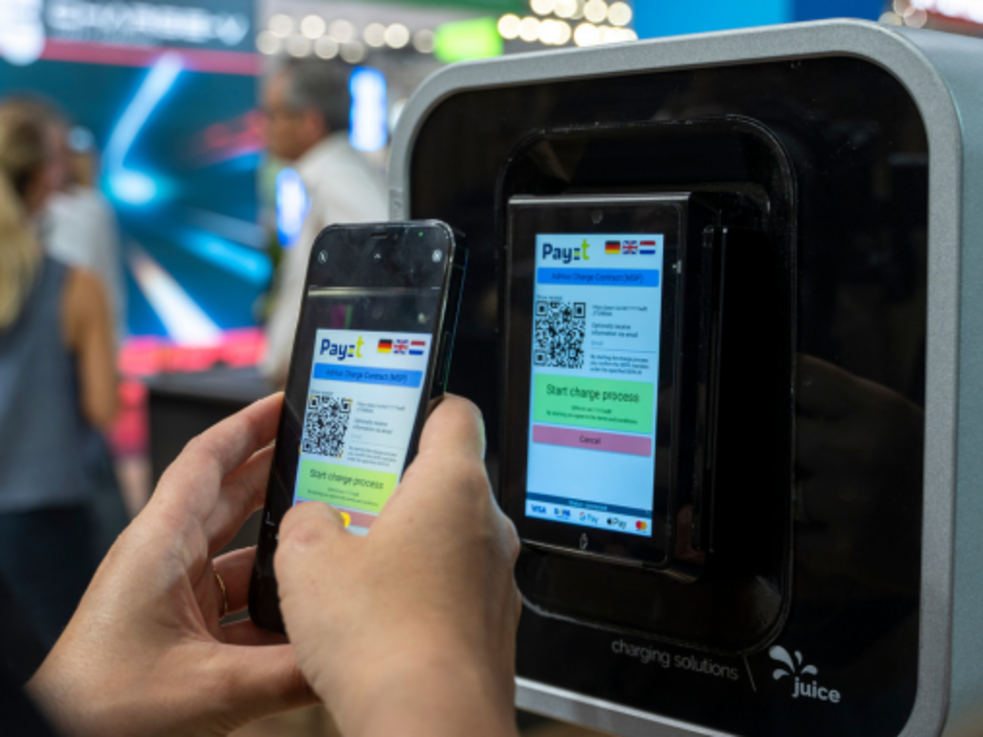 Eine Person scannt mit einem Smartphone an einer Ladestation einen QR-Code auf einem Bildschirm.