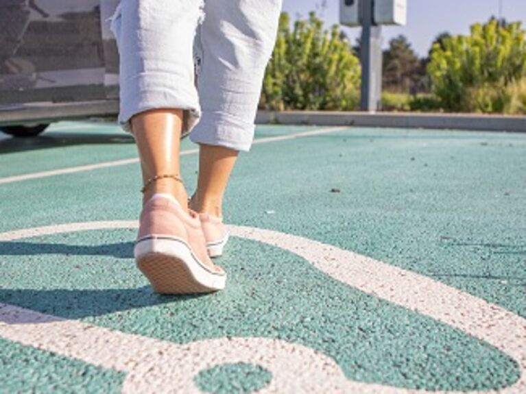 Person läuft über einen als für E-Fahrzeuge gekennzeichneten Parkplatz
